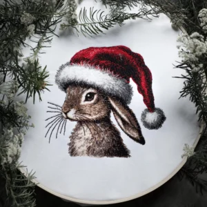 A detailed machine embroidery design of a realistic rabbit with lifelike fur texture, accented by a vibrant red Santa hat with intricate shading and fluffy white trim. Perfect for holiday décor or gifts, showcases high-quality stitching and depth.