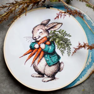 A vintage-style machine embroidery design featuring a charming woodland bunny in a green coat, joyfully holding a bundle of fresh carrots. The intricate stitchwork captures delicate fur textures, fine whiskers, and detailed shading, bringing the illustration to life with a nostalgic, storybook charm. Perfect for Easter, nursery decor, or heirloom projects, this whimsical design evokes the warmth of hand-painted illustrations in thread.
